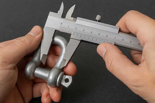 A person closely inspecting a steel shackle sample with calipers